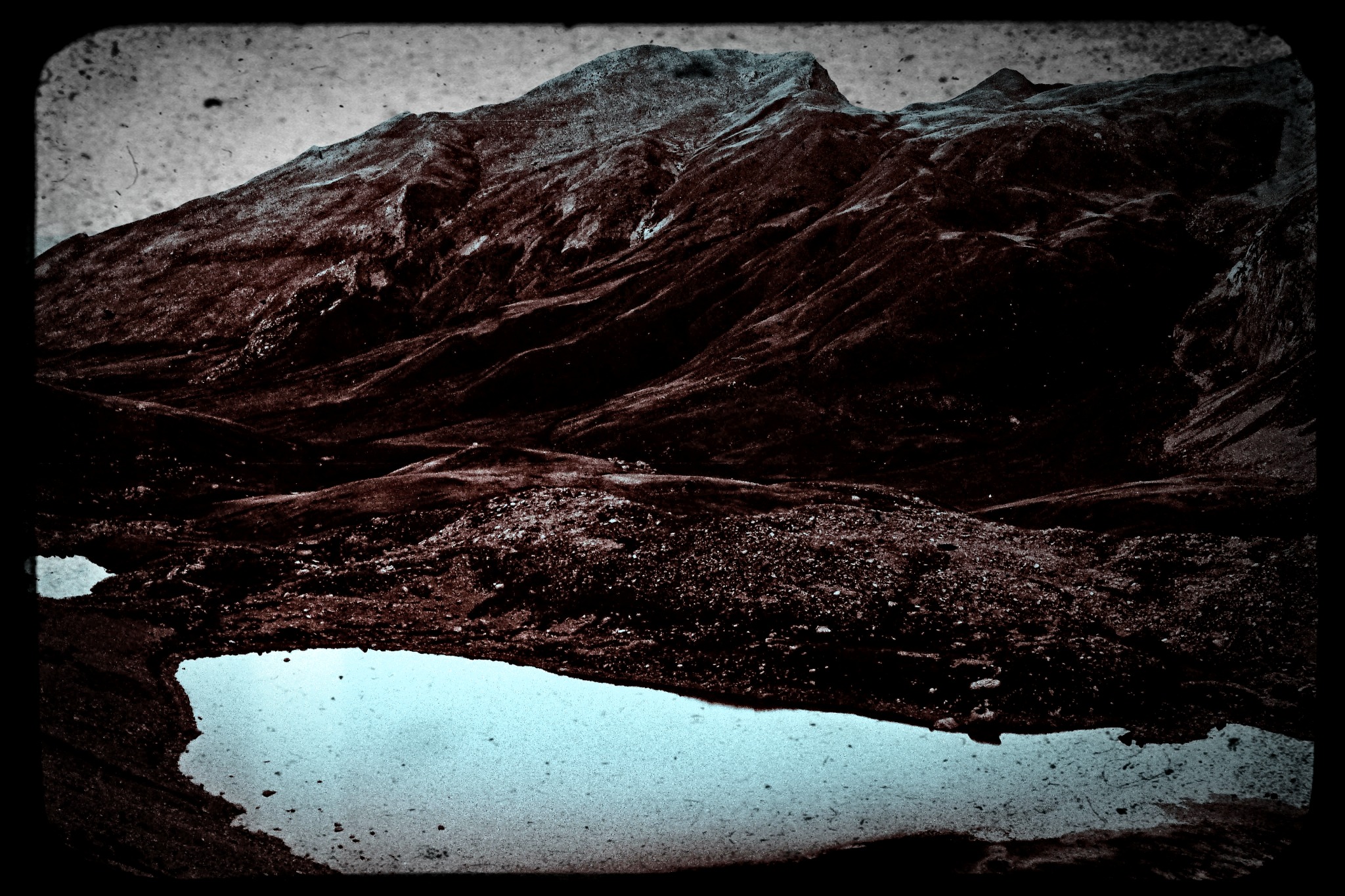 A dark, textured mountain landscape reflected in a pale blue pool